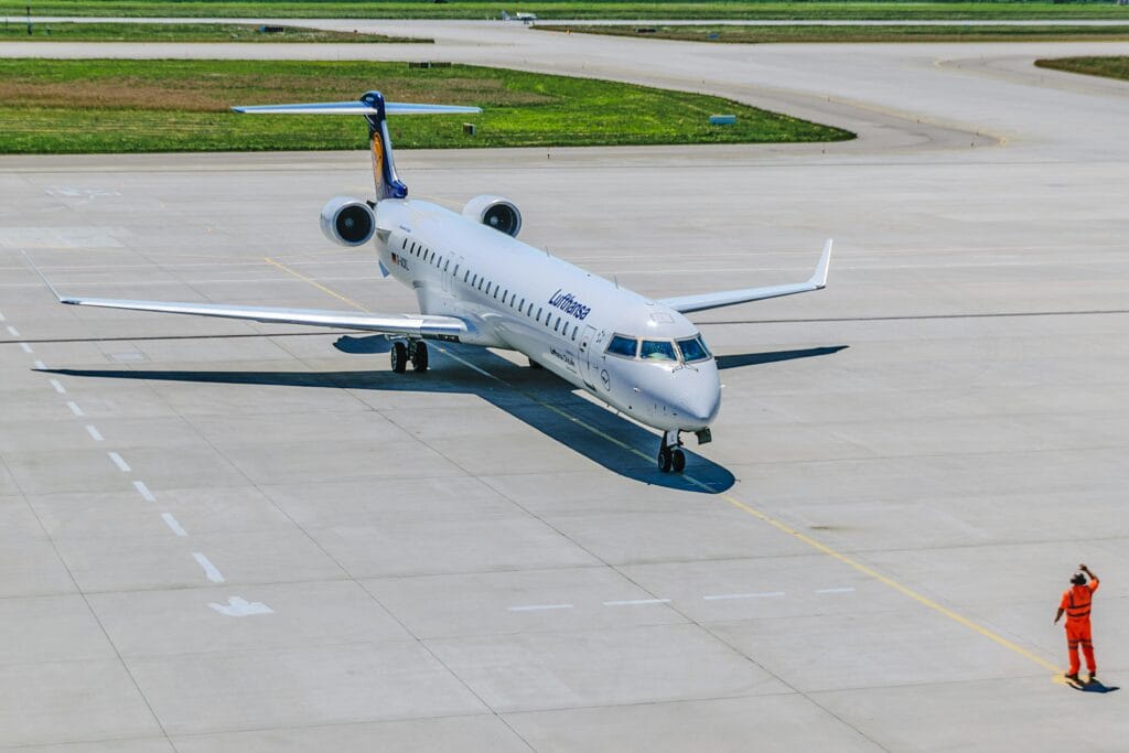 A Lufthansa airplane on the runway with an airport staff member directing traffic.