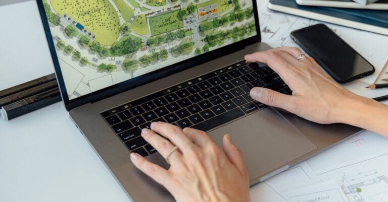 Architect working on landscape plan displayed on laptop with hands typing on keyboard.